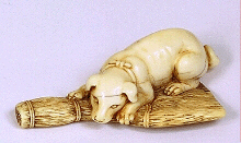 An 18th century Japanese ivory netsuke of a reclining dog resting on a besom